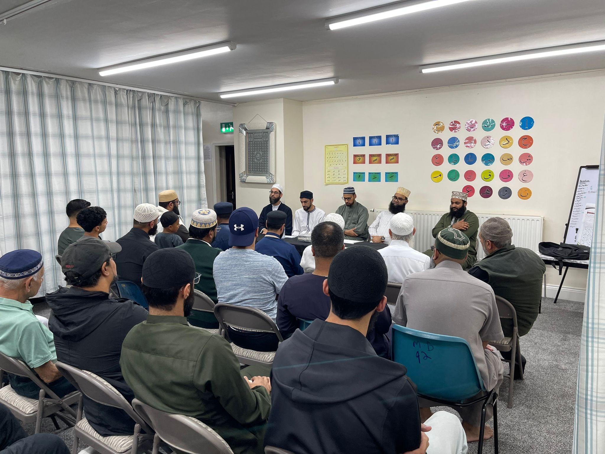 A full room of students facing a panel of five teachers seated at the front.